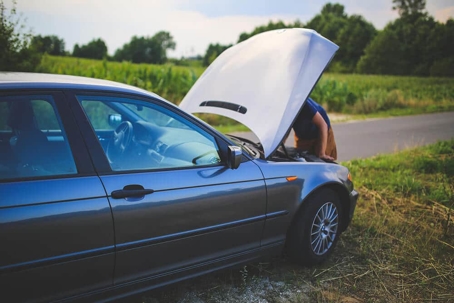 person looks under the hood of their car
