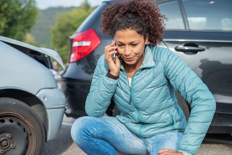 woman in blue jacket and jeans kneeled down on her phone after a car accident