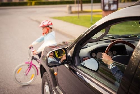 little girl riding bicycle in front of a moving vehicle