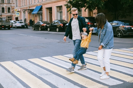 Mom and Dad walking across crosswalk swinging toddler