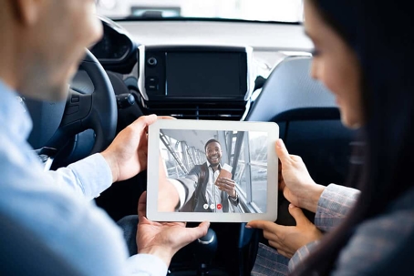 Man and woman in car doing a video conference with someone on iPad